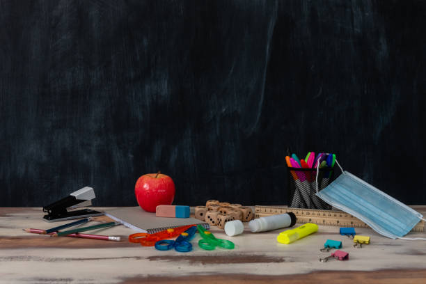 istock Classroom setting with a table and blackboard and various school supplies 1297871964