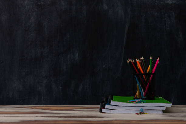 istock Classroom setting with a table and blackboard and various school supplies 1297872133