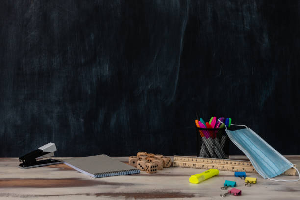 istock Classroom setting with a table and blackboard and various school supplies 1297872134