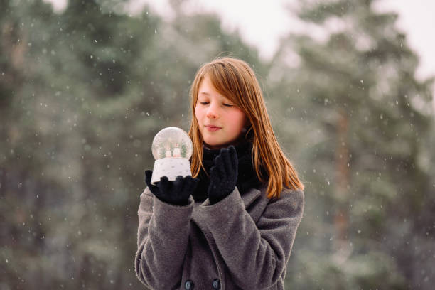 istock A young girl is holding a magic winter ball on a blurred forest background. 1297872922