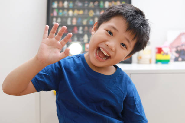 Little boy waving hand and talking to the camera video call Front view of a little Asian boy waving hand and talking to the camera video calling video conference with his friend and family during the pandemic lockdown. kid waves stock pictures, royalty-free photos & images