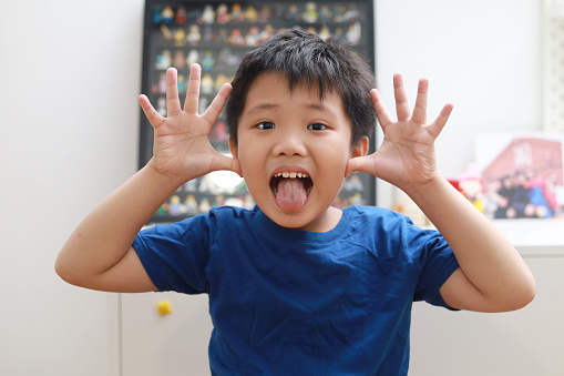 Front view of a little Asian boy making a face and talking to the camera video calling video conference with his friend and family during the pandemic lockdown.