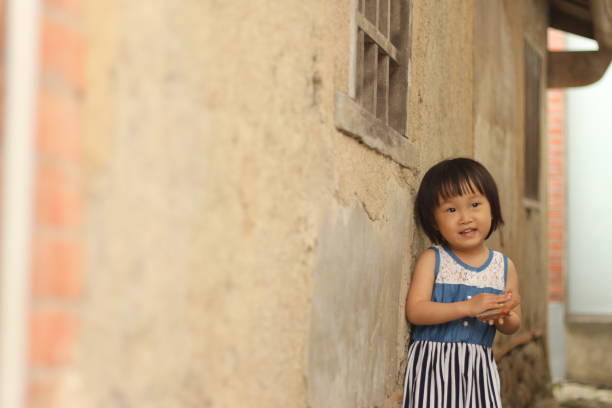 a Asian girl playing before an mottled old wall.