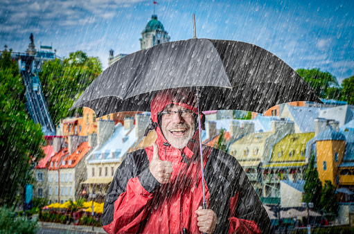 Happy man under rain with umbrella standing in front of Petit Champlain neighborhood downtown Quebec city