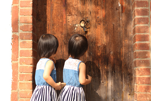 two smiling Asian girls playing and knocking an old wooden door. background for kindergarten and happy family.