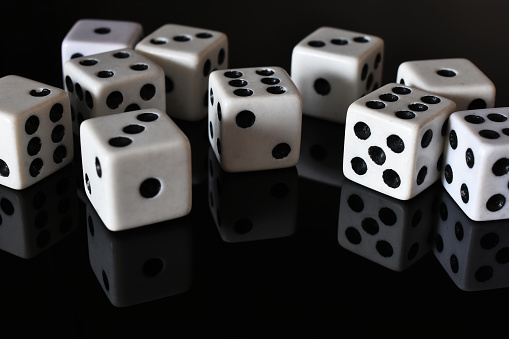 A close up image of several white dice on a black reflective table top.