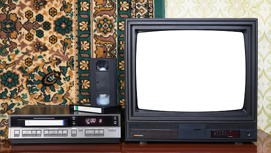Old black vintage TV with white screen to add new images to the screen, VCR against the background of old carpet and wallpaper.