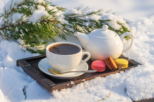 White cup of hot tea and teapot on a bed of snow and white background, close up. Concept of christmas winter morning