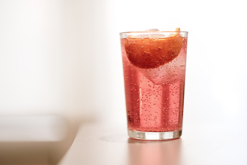 A gin tonic cocktail made with pink aromatic gin, and served with ice and a slice of orange
