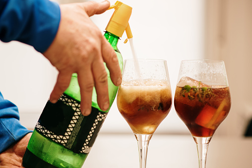 A bartender adding soda into vermouth glasses preparing a cocktail
