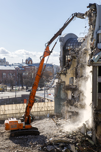 Building of the former hotel demolition for new construction, using a special hydraulic excavator-destroyer, city on background. Construction site, destruction concept