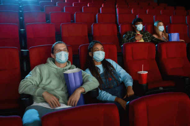 istock Cheerful young couple wearing face masks for protection from virus disease while watching movie in cinema auditorium 1297927120