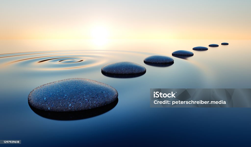 Stones in the ocean at sunrise Dark stones in calm water with evening sun with horizon - tranquil scenery Zen-like Stock Photo