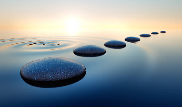 Stones in the ocean at sunrise Dark stones in calm water with evening sun with horizon - tranquil scenery buddhism stock pictures, royalty-free photos & images