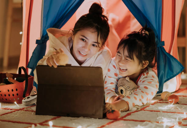 asiatico cinese mamma leggere storie alla figlia in un'accogliente tenda illuminata a casa - child digital tablet mother teaching foto e immagini stock