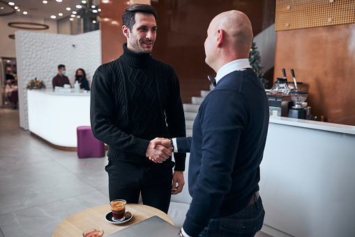 Cheerful male is celebrating success with business partner after working with laptop in hotel lobby