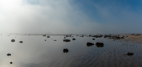 A panorama landscape of fog lifting over an endless wadden sea beach at low tide
