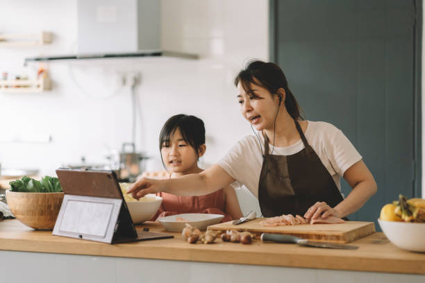 asiatico cinese madre insegnare figlia cucina seguendo le istruzioni online utilizzando tablet in cucina - child digital tablet mother teaching foto e immagini stock