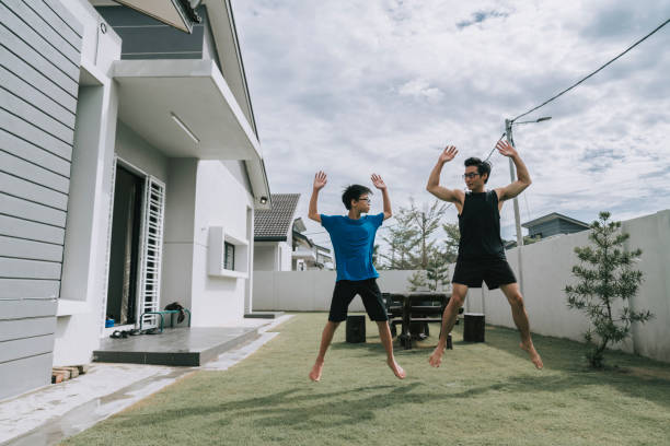 asian chinese teenager and his father doing jumping jacks exercise at backyard of the house father and son exercising at home Jumping Jacks stock pictures, royalty-free photos & images
