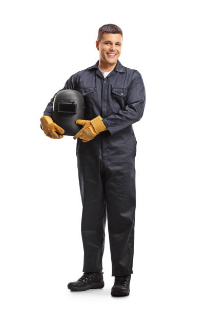 full length portrait of a welder in a uniform holding a protective helmet and smiling at camera - manual worker portrait helmet technology imagens e fotografias de stock