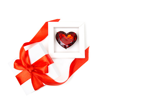 Large ruby colored heart shaped ring in a white box with a red bow and ribbon isolated on white. Romantic Valentine's day gift concept.