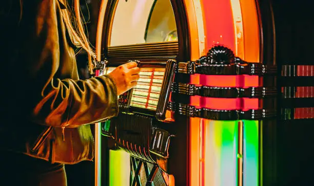 Photo of woman hand pushing buttons to play song on old Jukebox, selecting records