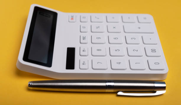 istock Calculator on yellow table with pen. Workplace of accountant, side view 1297941049