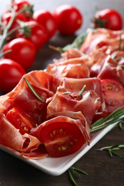 istock Prosciutto with  rosemary and tomato on a wooden table 1297941238