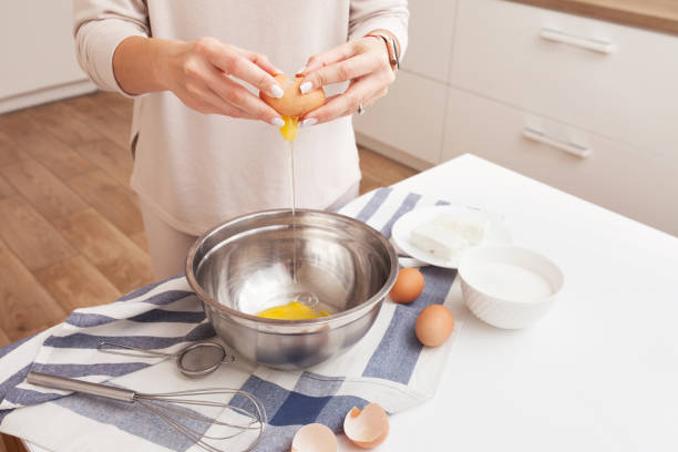 istock Woman cracking eggs into bowl. Hands holding an egg over a metal bowl 1297942906