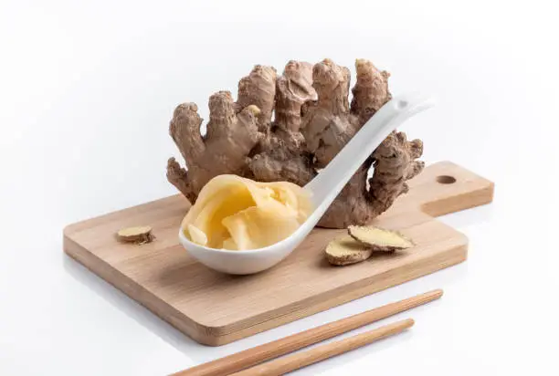 Gari or tsukemono is a Japanese pickled ginger  for sushi in a spoon with raw ginger root on white background, close up. Marinated ginger slices on a bamboo cutting board, tradition hot spices of Japanese and Asian cuisine.