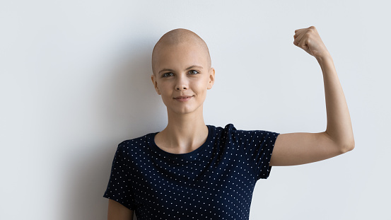 Strong powerful young female ill with cancer look at camera raise fist show biceps inspire to fight. Motivated sick hairless woman encourage oncology patients never give up. Studio portrait on white