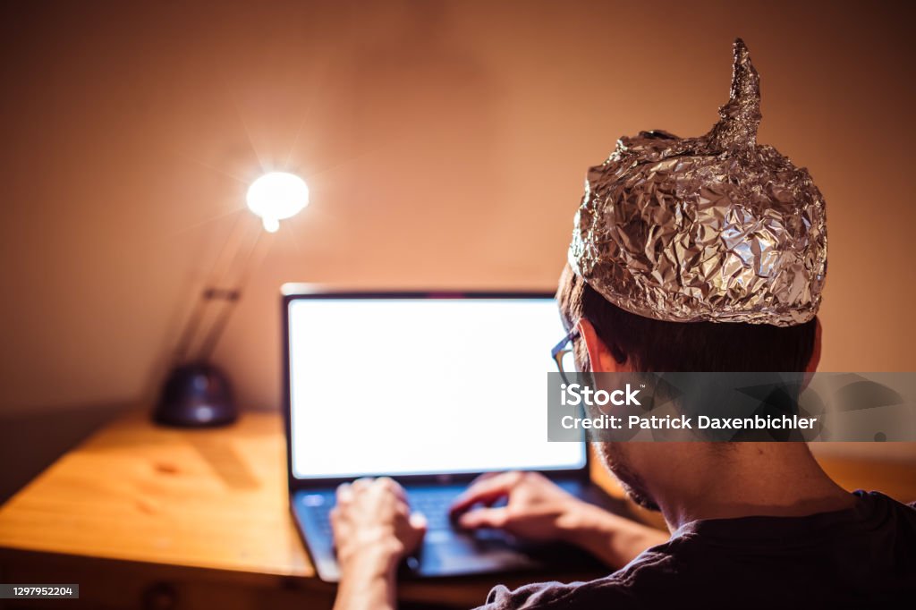 Conspiracy theory concept: young man with aluminum cap searching the internet, sitting lonely in the dark basement Young man with aluminum cap is sitting in the dark basement in front of a laptop. Conspiracy theory concept 30-34 Years Stock Photo