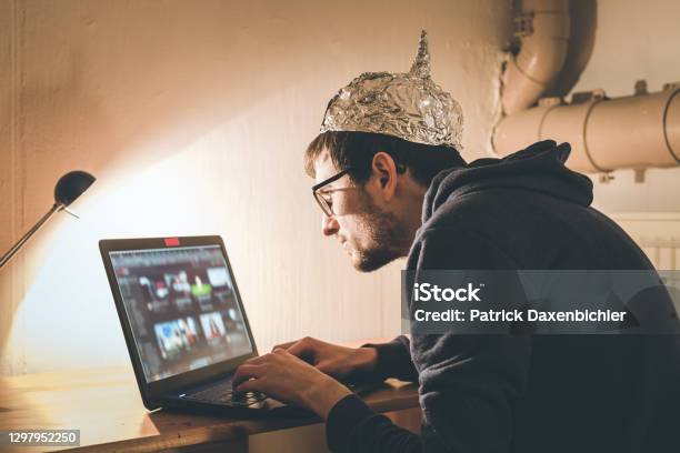 Conspiracy Theory Concept Young Man With Aluminum Cap Searching The Internet Sitting Lonely In The Dark Basement Stock Photo - Download Image Now
