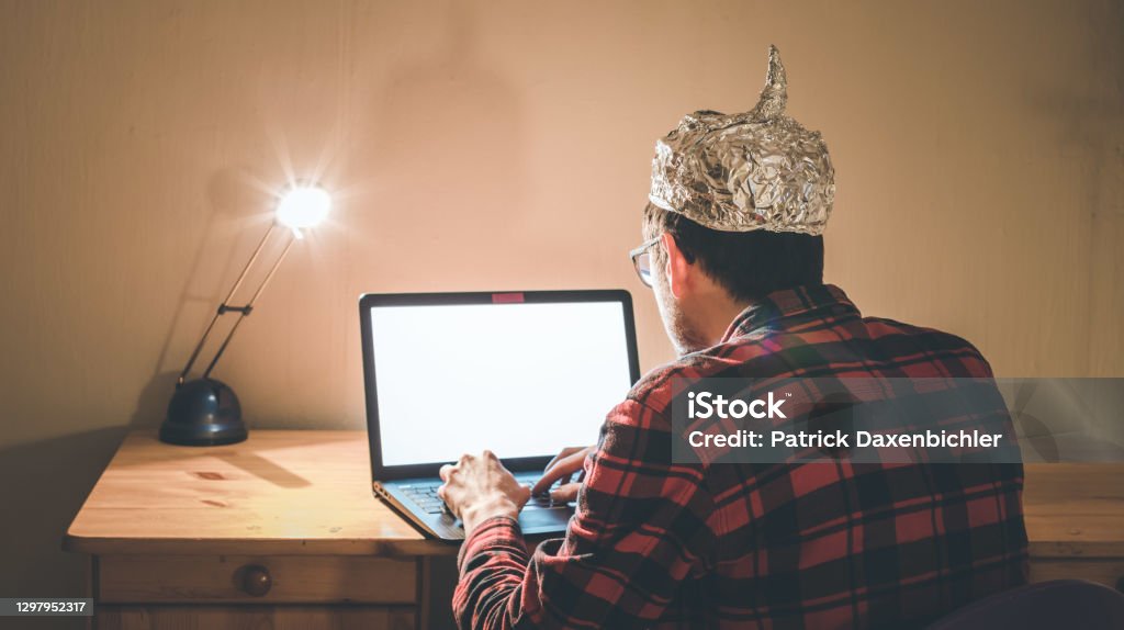 Conspiracy theory concept: young man with aluminum cap searching the internet, sitting lonely in the dark basement Young man with aluminum cap is sitting in the dark basement in front of a laptop. Conspiracy theory concept 30-34 Years Stock Photo