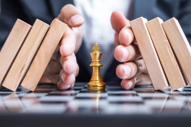 hombre de negocios proteger a mano figura de rey de ajedrez y detener la caída de bloques de madera o dominó. negocios, gestión de riesgos, solución, regresión económica, seguros, estrategia y conceptos de interrupción - strategy chess conflict chess board fotografías e imágenes de stock