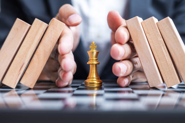 ビジネスマンの手はチェスキングの姿を保護し、木製のブロックやドミノの落下を停止します。ビジネス、リスク管理、ソリューション、経済回帰、保険、戦略、中断の概念 - risk management ストックフォトと画像