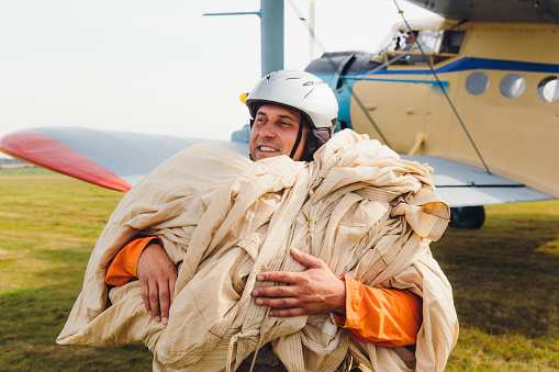 Happy smiling man in helmet and orange jacket landing from the flight  on the ground after parachuting