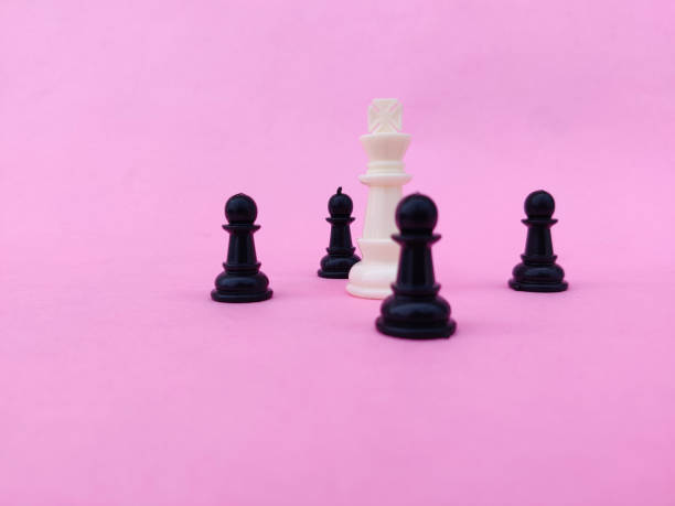 istock White chess king surrounded by black chess pawns. Isolated on pink background. 1297954676