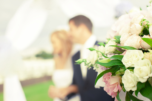 Beautiful bouquet of flowers on the background of a blurred silhouette of a loving couple of bride and groom.Focus on foreground, blurred background.