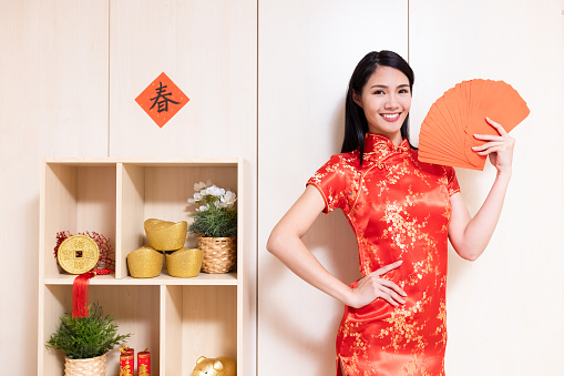 Asian pretty girl wearing cheongsam wish you a happy chinese new year with red envelops in hand