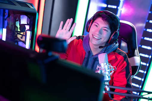 Smiling Young Asian Pro Gamer having live stream and playing Online Video Game