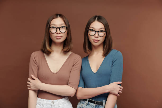 istock Serious twin sisters in pullovers and eyeglasses standing close to one another 1297961000