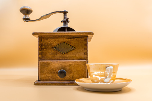 Old Coffee Mill with Small Vintage Shiny  Coffee Cup on Peach Background