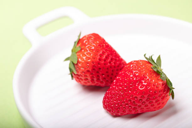 Stock photo showing close-up view of a whole bright red strawberry on a red surface, pictured against a mottled, dark blue background. The strawberry is a popular summer fruit that is considered to be an especially healthy snack 'super food', since they are packed with beneficial antioxidants and fibre, being a good source of vitamin C.