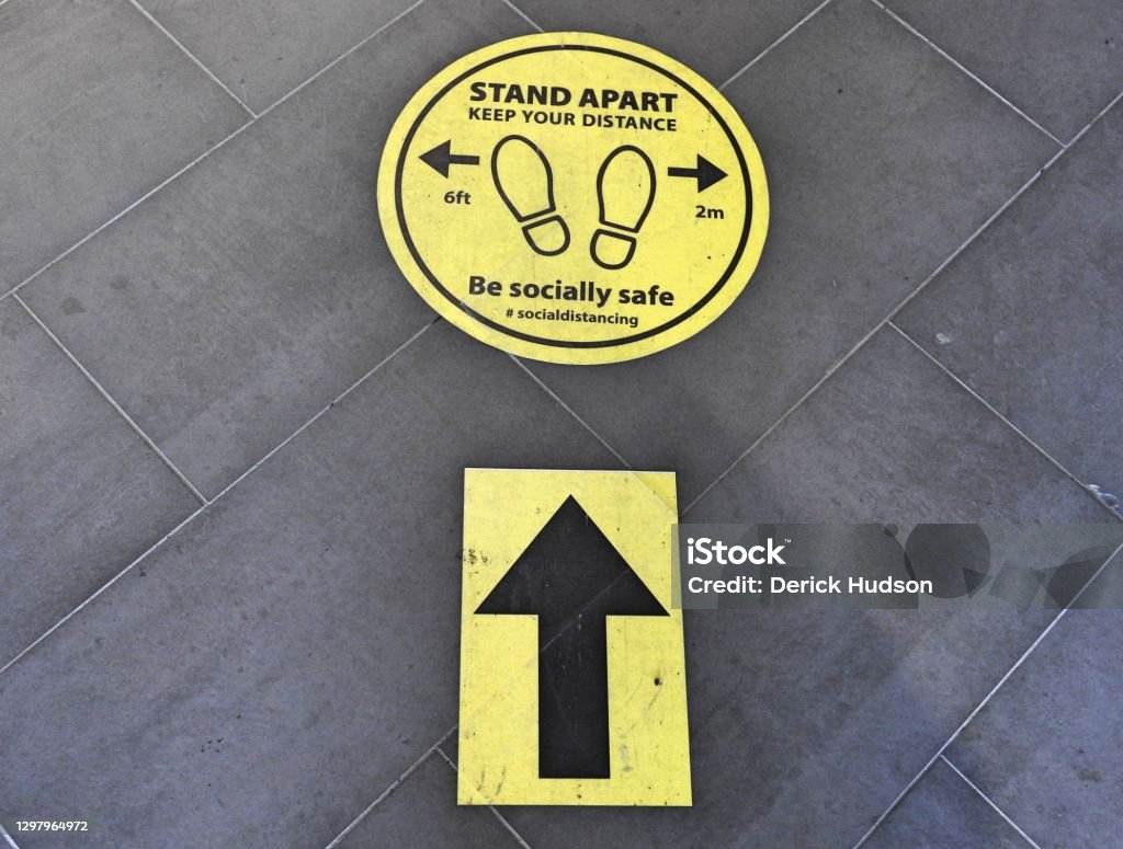 Socially distancing message Socially distancing directional pedestrian street ground sign. COVID-19 Stock Photo