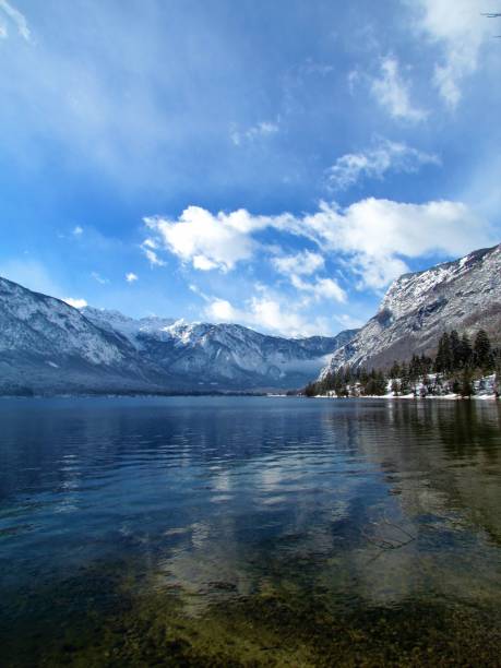 malerischer winterblick auf den bohinj-see in gorenjska, slowenien mit einer reflexion der berge und wolken im see und den bergen der julischen alpen dahinter - julian alps mountain lake reflection stock-fotos und bilder