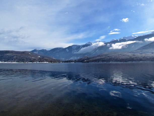 malerischer winterblick auf den bohinj-see in gorenjska, slowenien mit einer reflexion der berge und wolken im see und den bergen der julischen alpen dahinter - julian alps mountain lake reflection stock-fotos und bilder