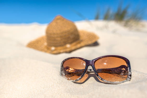 istock Background with summer vacation accessories on the beach, sunglasses and sun hat on sand dune and blue sky. 1297968732