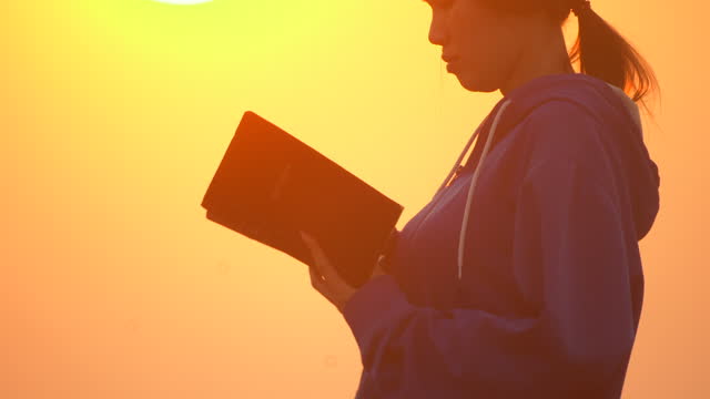 Girl reading bible outside at sunset