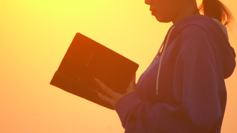 Girl reading bible outside at sunset